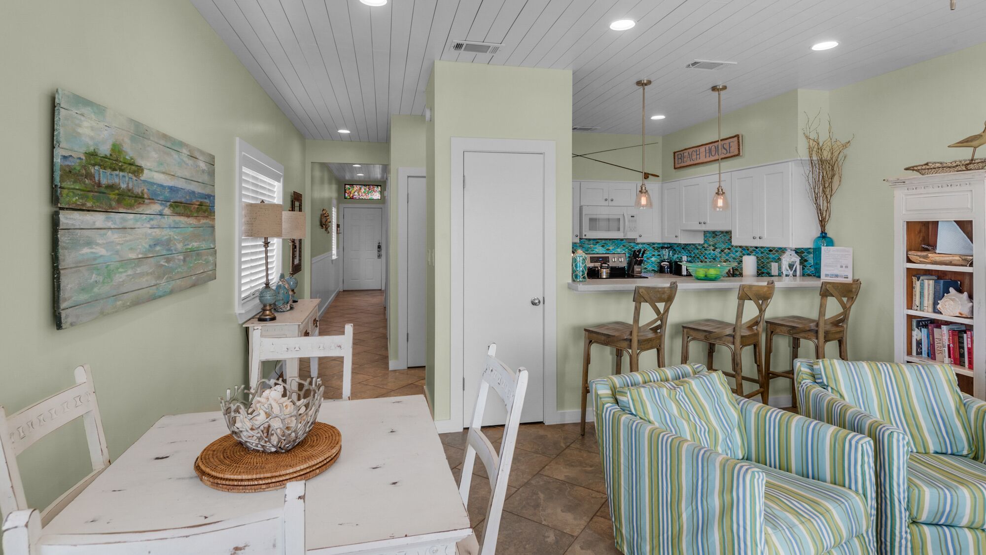 A cozy living room with a striped sofa, a dining table with chairs, and a kitchen area with white cabinets and a tiled backsplash.