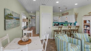 A cozy living room with a striped sofa, a dining table with chairs, and a kitchen area with white cabinets and a tiled backsplash. - Updated Gulf Front in Seagrove, Direct Sunset View + Free Attraction Tickets! (Santa Rosa Beach)