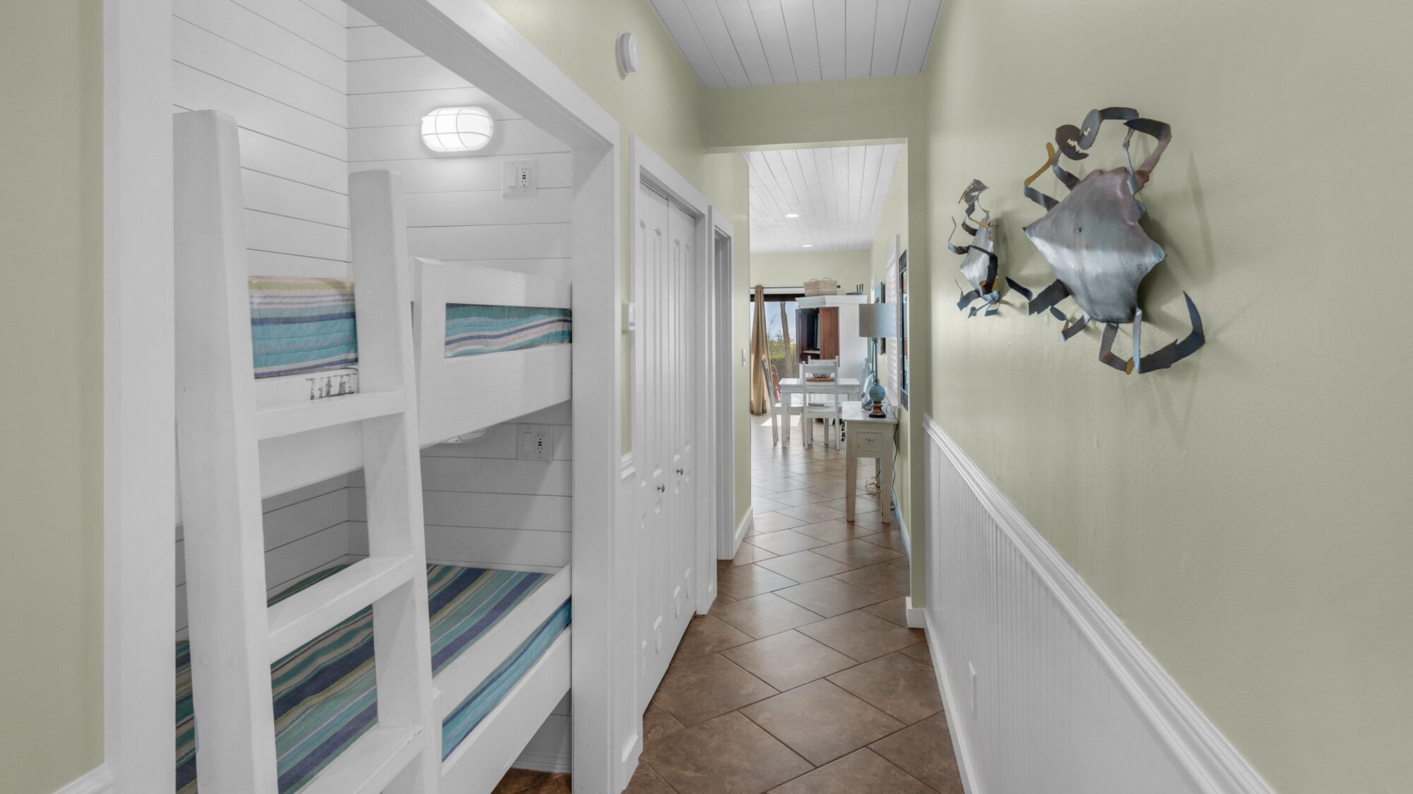 A hallway with white paneled walls, a dining area in the background, and a decorative shark artwork on the wall.
