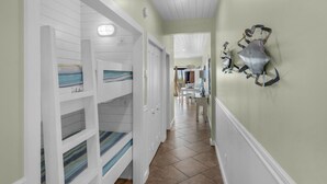 A hallway with white paneled walls, a dining area in the background, and a decorative shark artwork on the wall. - Updated Gulf Front in Seagrove, Direct Sunset View + Free Attraction Tickets! (Santa Rosa Beach)