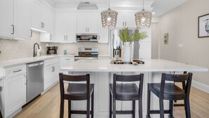 Una cocina moderna con armarios blancos, electrodomésticos de acero inoxidable y una isla central con taburetes de bar.