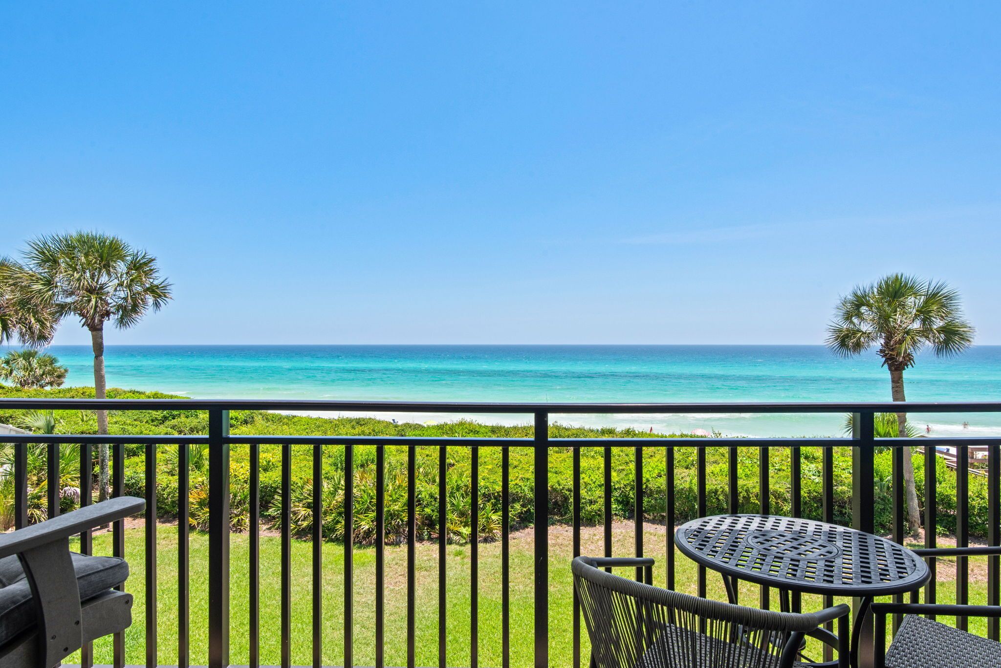 A balcony with a view of the ocean, a round table, and two chairs.