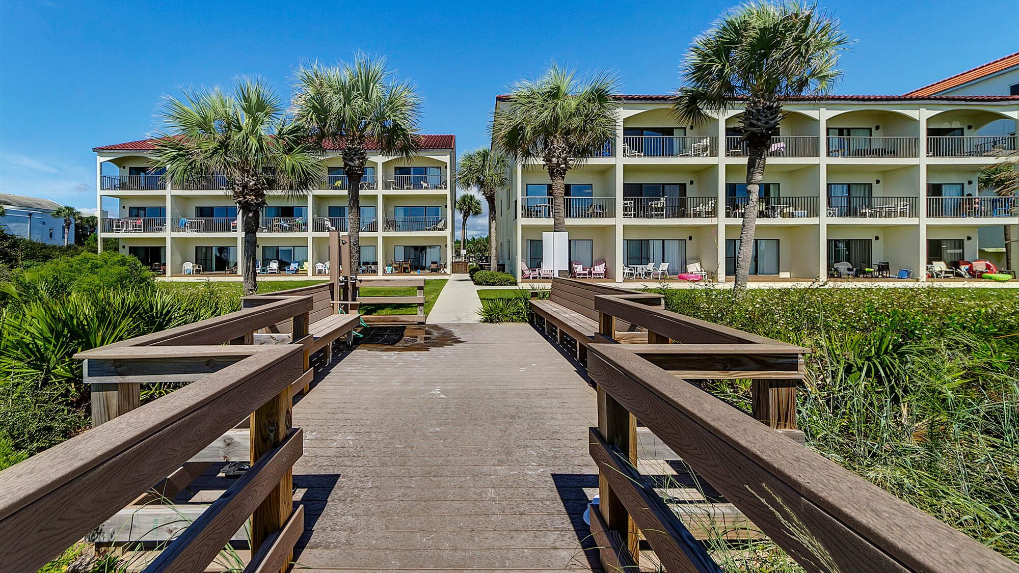 A resort with multiple-story buildings, outdoor seating areas, and a wooden boardwalk leading to the entrance.