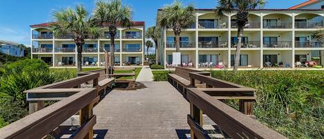 A resort with multiple-story buildings, outdoor seating areas, and a wooden boardwalk leading to the entrance.