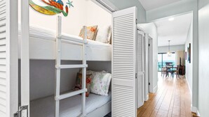 Een slaapkamer met stapelbed, een ladder, een deur met verstelbare luiken en een gang naar een eetruimte.