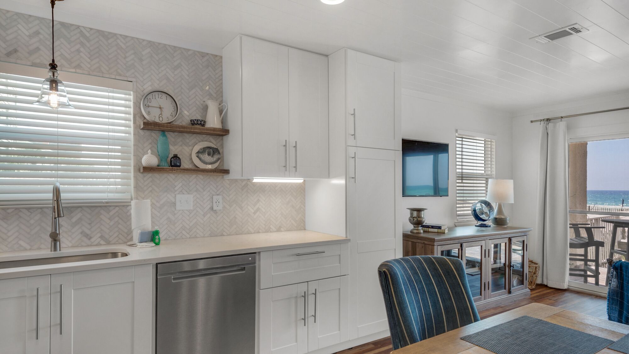 A modern kitchen with white cabinets, a stainless steel dishwasher, and a dining area with a table and chairs.