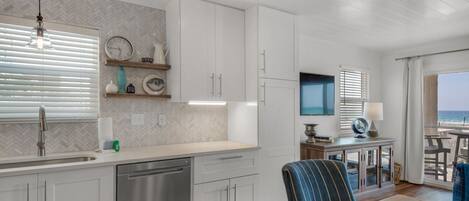 A modern kitchen with white cabinets, a stainless steel dishwasher, and a dining area with a table and chairs.