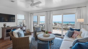 A spacious living room with a large window overlooking a beach, furnished with wicker chairs, a sofa, and a small round table. - Direct Gulf views & access to the sparkling waters + Free Attraction Tickets! (Santa Rosa Beach)
