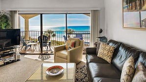 A living room with a leather sofa, a beige armchair, and a television. There is a balcony with a view of the ocean. - Gulf-Front, Pool in Seagrove, Next Door to Seaside + Free Attraction Tickets! (Santa Rosa Beach)