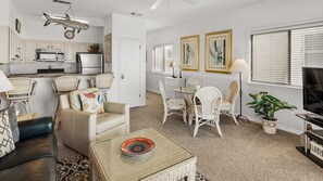 A living room with a sofa, chairs, a dining table, and a kitchen area with cabinets and appliances.