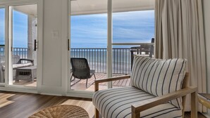 A room with a view of the ocean, a wicker chair, a striped sofa, and a wooden floor.