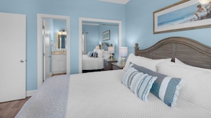 A bedroom with a large bed, a wooden headboard, a nightstand with a lamp, and a painting on the wall.