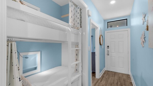A room with bunk beds, a window, a door, and a hallway.