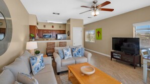 A living room with a sofa, coffee table, TV, and a kitchen in the background.