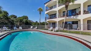 A swimming pool with lounge chairs and a multi-story building with balconies.