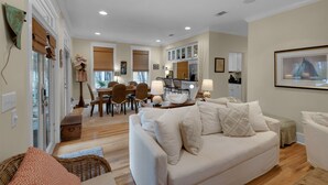 A spacious living area with a sofa, dining table, and chairs. There is a kitchen area with cabinets and a countertop. - Dog-Friendly Gulf Side Cottage, 6 Mins to Beach, Pool, Bikes + Free Tickets! (Santa Rosa Beach)