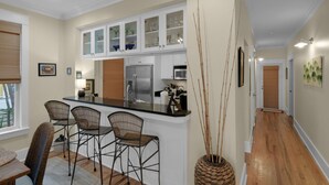 A kitchen with a central island, white cabinets, and a microwave. There are three wicker chairs and a vase with tall stems. - Dog-Friendly Gulf Side Cottage, 6 Mins to Beach, Pool, Bikes + Free Tickets! (Santa Rosa Beach)