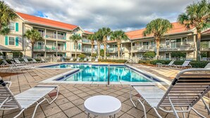 A pool area with lounge chairs and a small table, surrounded by multi-story buildings with balconies and palm trees. - Ground Floor, Complex Pool, Near to Beach & Dining + Free Attraction Tickets! (Santa Rosa Beach)