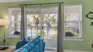 Une pièce comprenant un canapé, une lampe et une vue sur une piscine et des palmiers, visible à travers une porte-fenêtre coulissante.