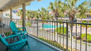 Un balcon avec des chaises turquoise, une piscine et des palmiers.