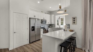 Una cocina moderna con armarios blancos, electrodomésticos de acero inoxidable y una isla central con taburetes de bar.