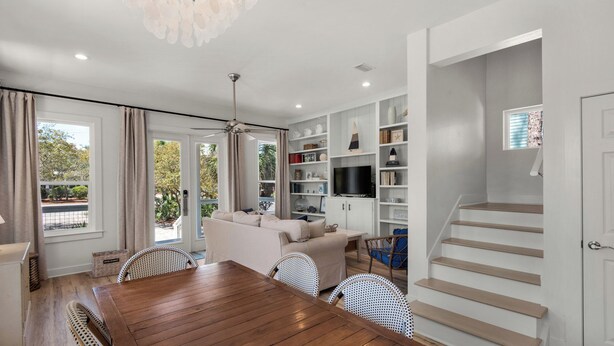 Un moderno salón con una mesa de comedor de madera, sofás blancos y un televisor sobre un estante blanco.