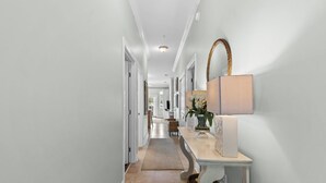 A hallway with a light-colored floor, white walls, and a white console table with a lamp and decorative items. - Coastal Condo for 6 w/ Pool, 6 Mins to the Beach + Free Attraction Tickets! (Santa Rosa Beach)