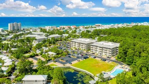 An aerial view of a resort with a swimming pool, parking area, and buildings surrounded by greenery and the ocean. - Coastal Condo for 6 w/ Pool, 6 Mins to the Beach + Free Attraction Tickets! (Santa Rosa Beach)
