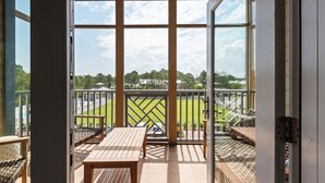 A balcony with a view of a green field and a pool, wooden furniture, and a ceiling fan. - Coastal Condo for 6 w/ Pool, 6 Mins to the Beach + Free Attraction Tickets! (Santa Rosa Beach)