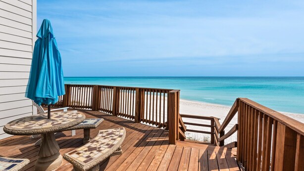 A wooden deck with a table and chairs, a blue umbrella, and a view of the beach. - Gulf Front, Steps to Beach, Sleeps 11 + Attraction Tickets! (Inlet Beach)