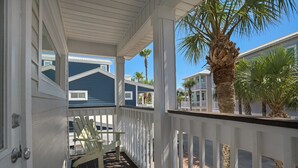 Een overdekte veranda met een witte balustrade, een stoel en een palmboom.