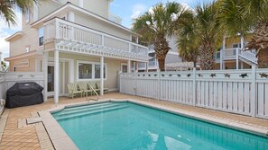 A pool area with a white fence, a covered grill, and outdoor seating.