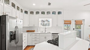 Una cocina moderna con armarios blancos, un refrigerador de acero inoxidable, una estufa a gas y una ventana con vistas.