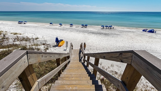Een houten trap die uitkomt op een strand met parasols en ligstoelen.