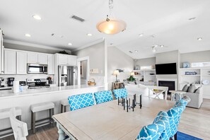 Una cocina moderna con armarios blancos, una isla central y un comedor con sillas de diseño azul.