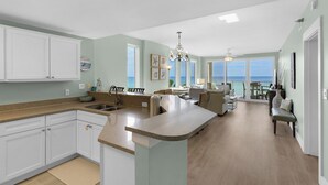 Una cocina amplia con una isla grande, armarios blancos y vista al océano.