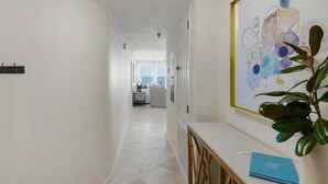 A hallway with a view to a balcony, a framed abstract painting, and a blue book on a counter. - Gulf Front, Pool, Modern Design & Amazing Views + Free Attraction Tickets! (Seacrest)