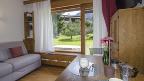 Un cuarto acogedor con un sofá, una mesa de comedor con una cafetera, un florero con flores y vistas a un paisaje verde a través de grandes ventanales.
