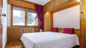 Un dormitorio con cabecera de madera, una ventana con cortinas y una cama con sábana blanca.