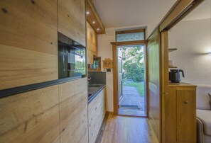 A narrow hallway with wooden walls, a kitchen area with a sink, and a door leading to an outdoor area.