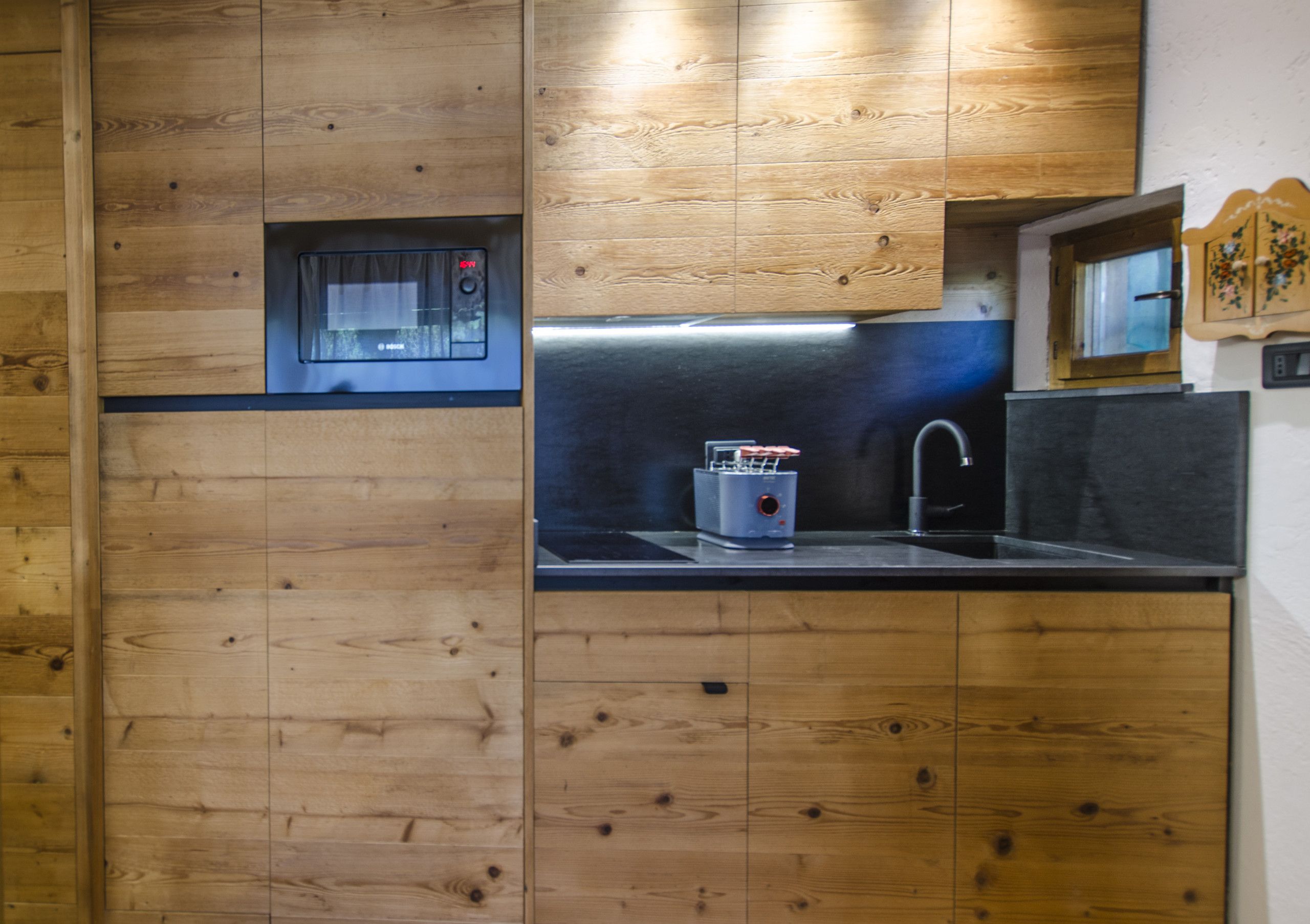 A compact kitchen with wooden cabinetry, a built-in microwave, and a stainless steel sink.