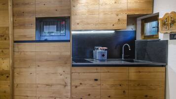 A compact kitchen with wooden cabinetry, a built-in microwave, and a stainless steel sink.