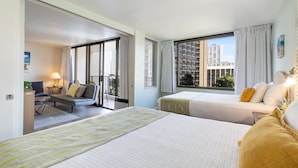 Quarto de hotel com duas camas, um sofá, uma mesa de trabalho e vista para a paisagem urbana.