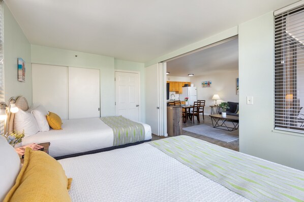 A hotel room with two beds, a desk, and a kitchenette.