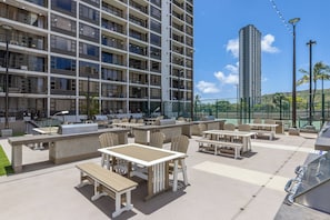 A rooftop patio with outdoor seating, a barbecue area, and a view of a high-rise building.