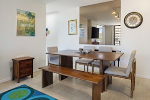 Un coin repas comprenant une table en bois, quatre chaises, un banc, une petite table d’appoint en bois et une horloge murale.