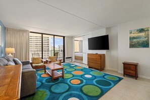 A modern hotel room with a large TV, a sofa, a coffee table, a wooden cabinet, and a colorful rug. - Spacious 14th Floor Corner Suite, Partial Diamond Head and Ocean Views, FREE Parking! (Honolulu)