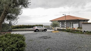 A house with a gravel driveway, a parked car, and a view of the sea. - Villa Antonio (Aci Castello)