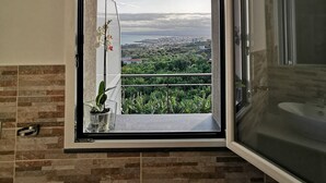 A bathroom with a large window offering a cityscape view. - Villa Antonio (Aci Castello)