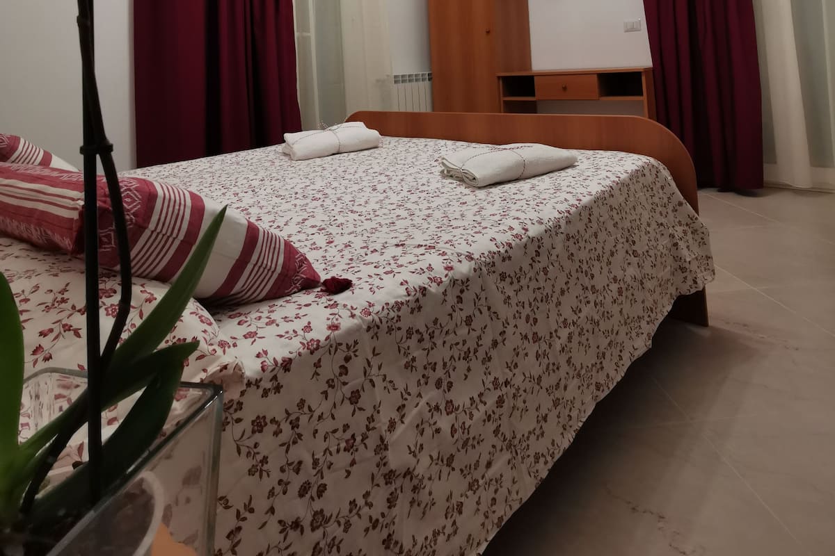 Habitación de hotel con cama, televisor, armario de madera y una orquídea en maceta.